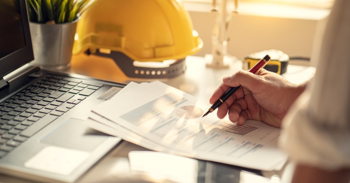 A contractor and a client reviewing blueprints together inside a partially framed residential construction site.