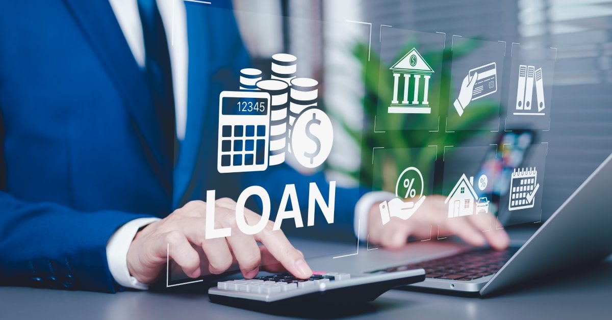 A man in a blue suit pressing a calculator while digital loan icons float beside a laptop on his desk.