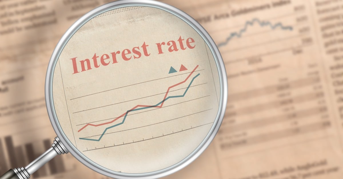  A magnifying glass held over a newspaper shows a chart labeled 'Interest rate' with two rising lines and triangle markers.