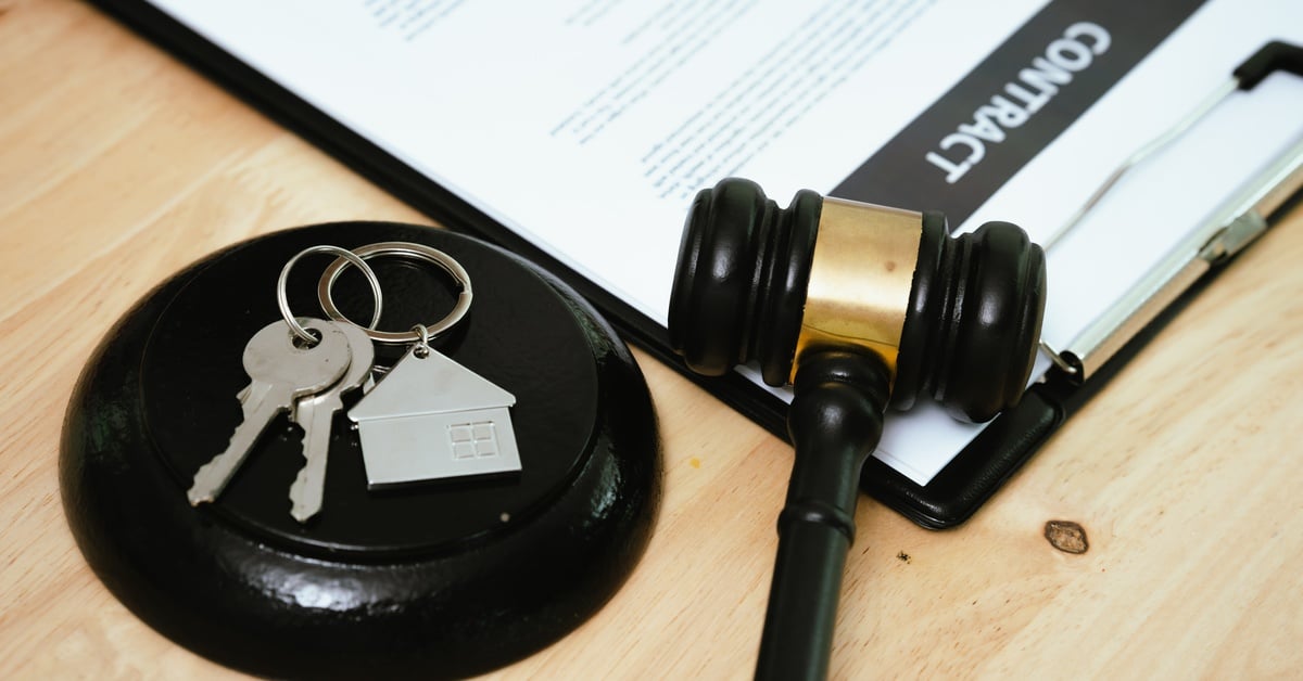 A close-up of a contract on a clipboard with a judge’s gavel and a set of house keys on a keychain placed beside it.