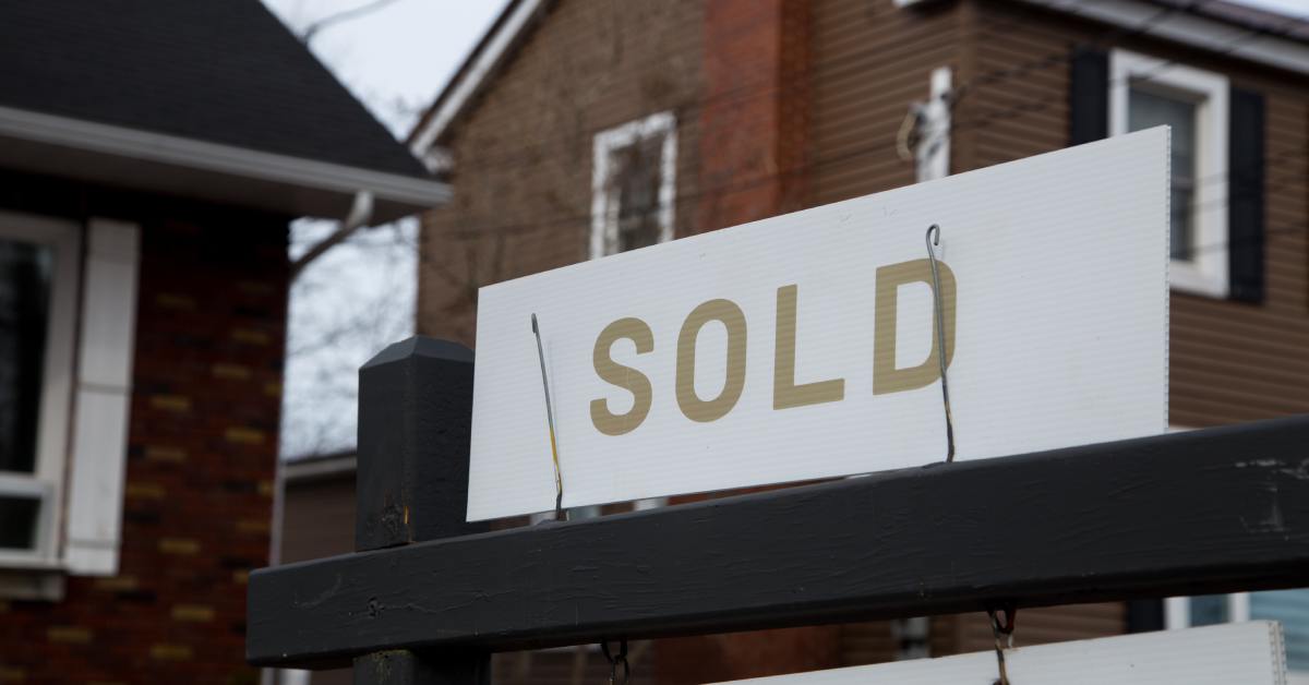 A close-up of a real estate sign that says "SOLD". It's outside of a suburban house, representing a completed home purchase.