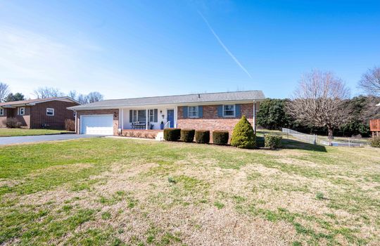 brick ranch, paved driveway, yard, landscaping, front door, front porch, garage
