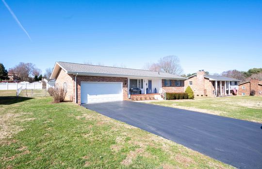 brick ranch, paved driveway, yard, landscaping, front door, garage