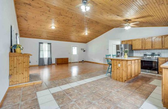 kitchen, kitchen island, tile flooring, cabinets, counters, stainless appliances, vaulted wood ceiling, ceiling fan