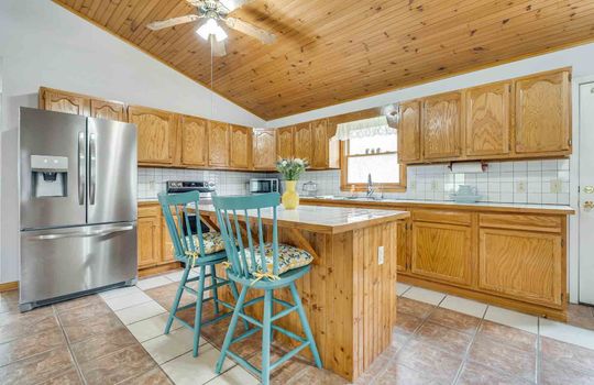 kitchen, kitchen island, tile flooring, cabinets, counters, stainless appliances, vaulted wood ceiling, ceiling fan, kitchen sink