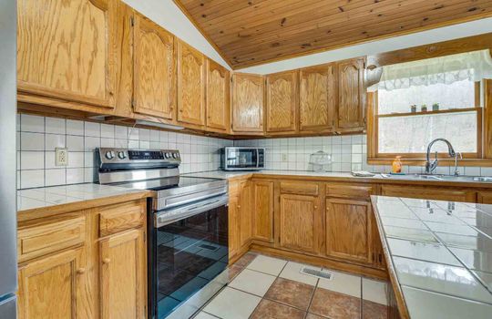 kitchen, kitchen island, tile flooring, cabinets, stove, refrigerator, vaulted wood ceiling, tile backsplash, sink, window