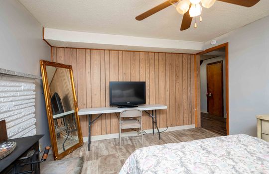 bedroom, ceiling fan, vinyl flooring, paneling wall, doorway, fireplace