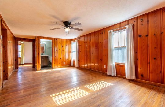 living room, paneling walls, hardwood flooring, ceiling fan, door to full bath