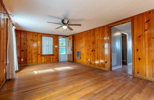 living room, paneling walls, hardwood flooring, ceiling fan, front door