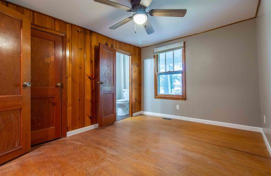 primary bedroom, hardwood flooring, ceiling fan, paneling accent wall, half bath