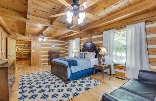 bedroom, wood walls, wood flooring. log walls, ceiling fan, window