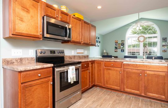 kitchen, cabinets, stove/oven, built-in microwave, laminate flooring, view into living room.