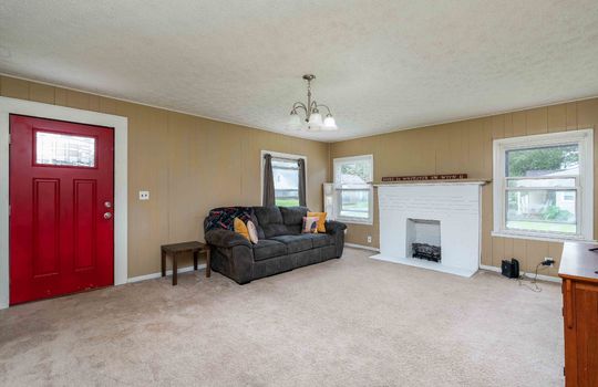 living room, chandelier, carpet flooring, painted paneling walls, painted brick fireplace, windows