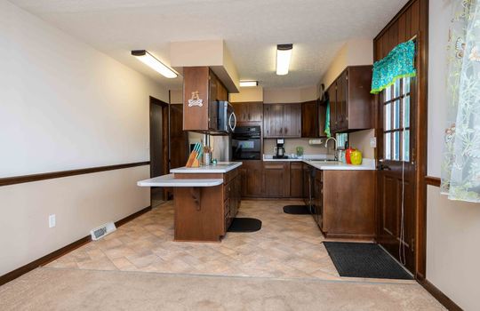 kitchen, kitchen island, microwave, in wall oven, cooktop, dishwasher, cabinets, counters, door to back deck, vinyl flooring