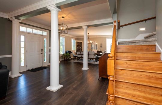 view from sitting area into entryway/stairs/dining area, columns, front door, chandelier, steps, crown moulding, wainscoting