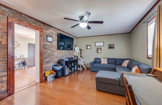 den, brick accent wall, hardwood flooring, ceiling fan