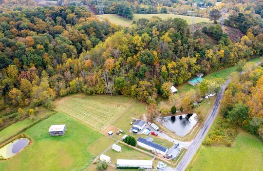 aerial view of property, singlewide, pond, fenced pasture, trees, gravel drive, two bay garage