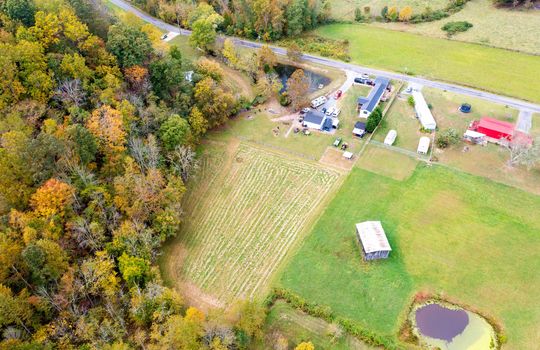 aerial view of property, fenced pasture, wooded area, singlewide, pond, two bay garage, gravel driveway