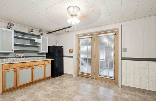 Lower level kitchen area, refrigerator, cabinets, sink, vinyl flooring, double doors
