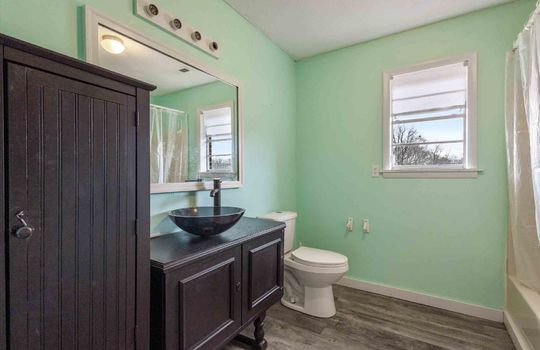 bathroom, luxury vinyl flooring, tub/shower, toilet, sink, linen cabinet, vanity lighting, window