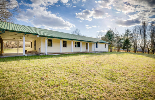 Left side view of home, ranch style home, front yard, front door, covered front porch, metal roof, covered patio/carport, trees