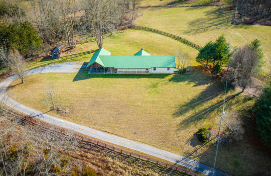 aerial view of primary home, green metal roof, driveway, fence, trees