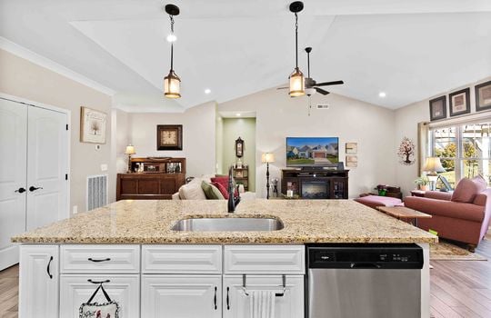 kitchen view into living room, vaulted ceilings, pendant lights, ceiling fan, kitchen island with sink and dishwasher, luxury vinyl flooring, recessed lighting