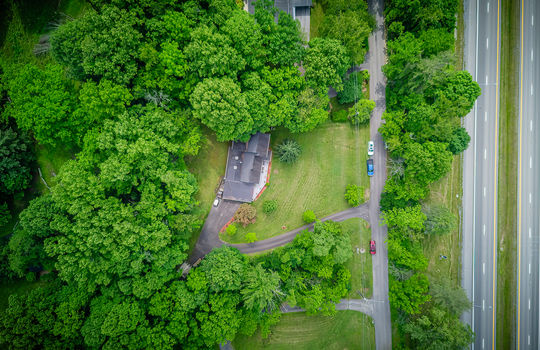 aerial view of property, driveway, road, roof, front yard, back yard, trees