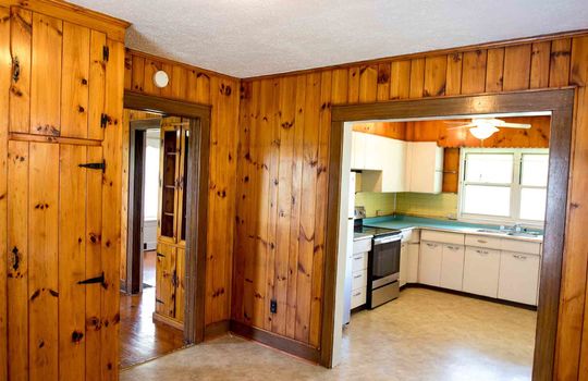 living room, knotty pine walls, laminate flooring, doorway into kitchen, kitchen cabinets, oven/range