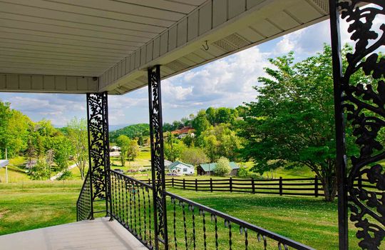 view from covered back porch, railing, fencing, barn, back. yard, trees, mountain views