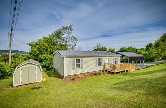 Double wide, manufactured home, front porch, ramp, front door, yard, carport, metal roof, vinyl siding, landscaping, storage shed