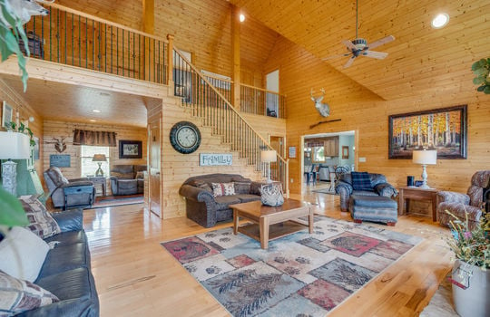 living room, hardwood flooring, wood walls, vaulted wood ceiling, wood stairs to upper level, ceiling fans