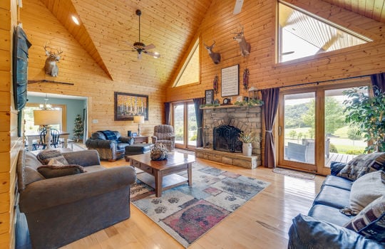 living room, fireplace, hardwood flooring, wood walls, wood vaulted ceiling, large windows, ceiling fans