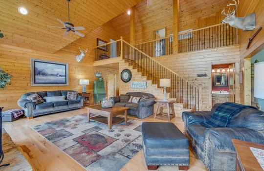 living room, hardwood flooring, wood walls, vaulted wood ceiling, wood stairs to upper level, ceiling fans