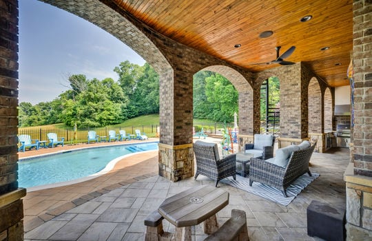 lower level patio, patio pavers, brick home exterior, outdoor fan, view toward swimming pool