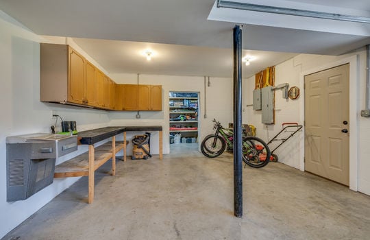 garage, concrete flooring, work bench, cabinets, door