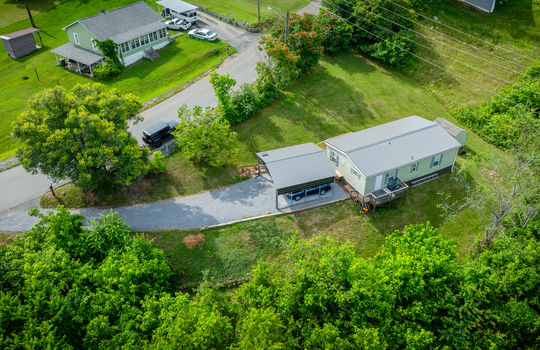 aerial view of home, carport, doublewide, metal roof, gravel drive, road, trees, front yard, back yard