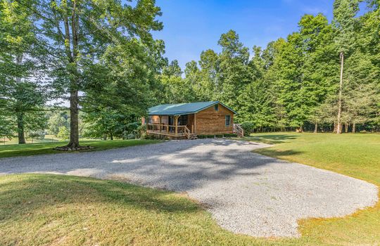 gravel driveway, log cabin, for lease only, metal roof, covered front porch, trees, yard