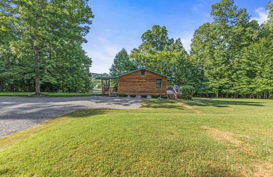 side view of log cabin, for lease only, driveway, yard, trees,