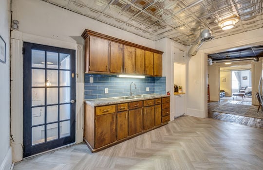 Kitchen, herringbone floor patter, cabinets, countertops, sink, tile backsplash, view into dining area