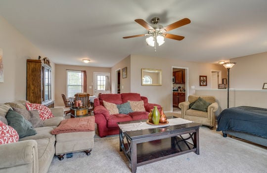 living room view toward dining area, carpet, ceiling fan, door to kitchen, dining area