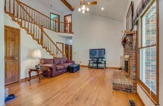 living room, fireplace, stairs to upper level, hardwood flooring, ceiling fan, vaulted ceilings