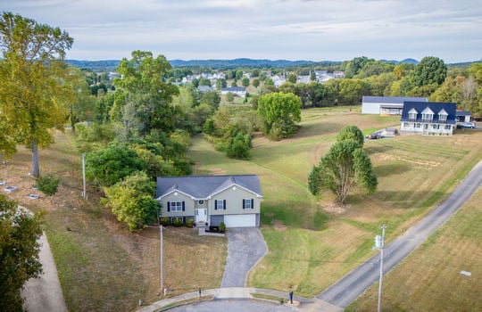 aerial view of home, front yard, driveway, split level home, garage, vinyl siding, roof, trees, landscaping, sidewalk, mountains