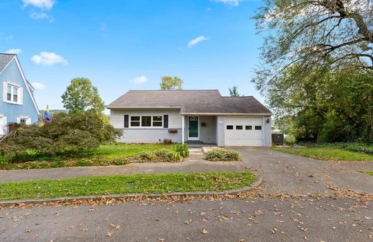 street view of home, cottage, house, vinyl siding, brick, garage, driveway, garage door, front door, window, roof, landscaping, sidewalk