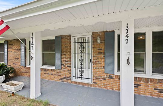 covered front porch, storm door, front door, brick exterior, windows