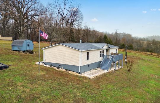 back side view, double wide, vinyl siding, back deck, metal roof, flag pole, landscaping, back yard, trees, mountain views