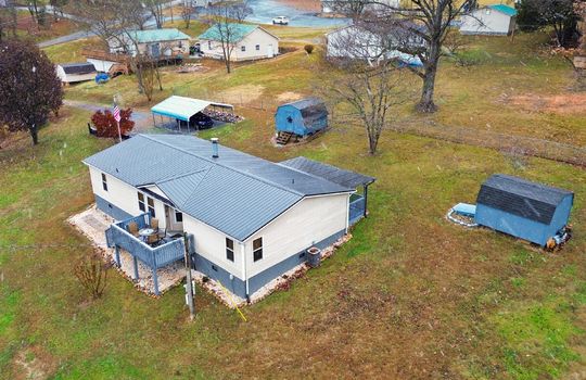 aerial photo from back of property, metal roof, vinyl siding, double wide, back deck, covered front porch, back yard, front yard, storage sheds, carport, neighboring properties