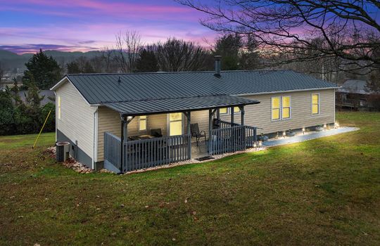 twilight photo, double wide, vinyl siding, covered front porch, metal roof, ramp access to porch, front yard, landscaping, trees, mountain views