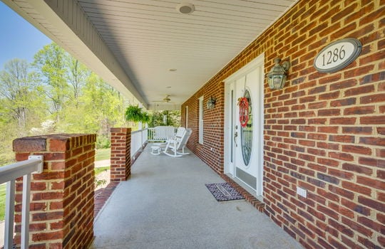 covered front porch, ceiling fan, lighting, front door, brick home exterior, steps, trees, front yard