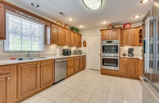 kitchen, dishwasher, sink, double wall oven, refrigerator, tile flooring, window above sink, cabineets, countertops, recessed lighting, door